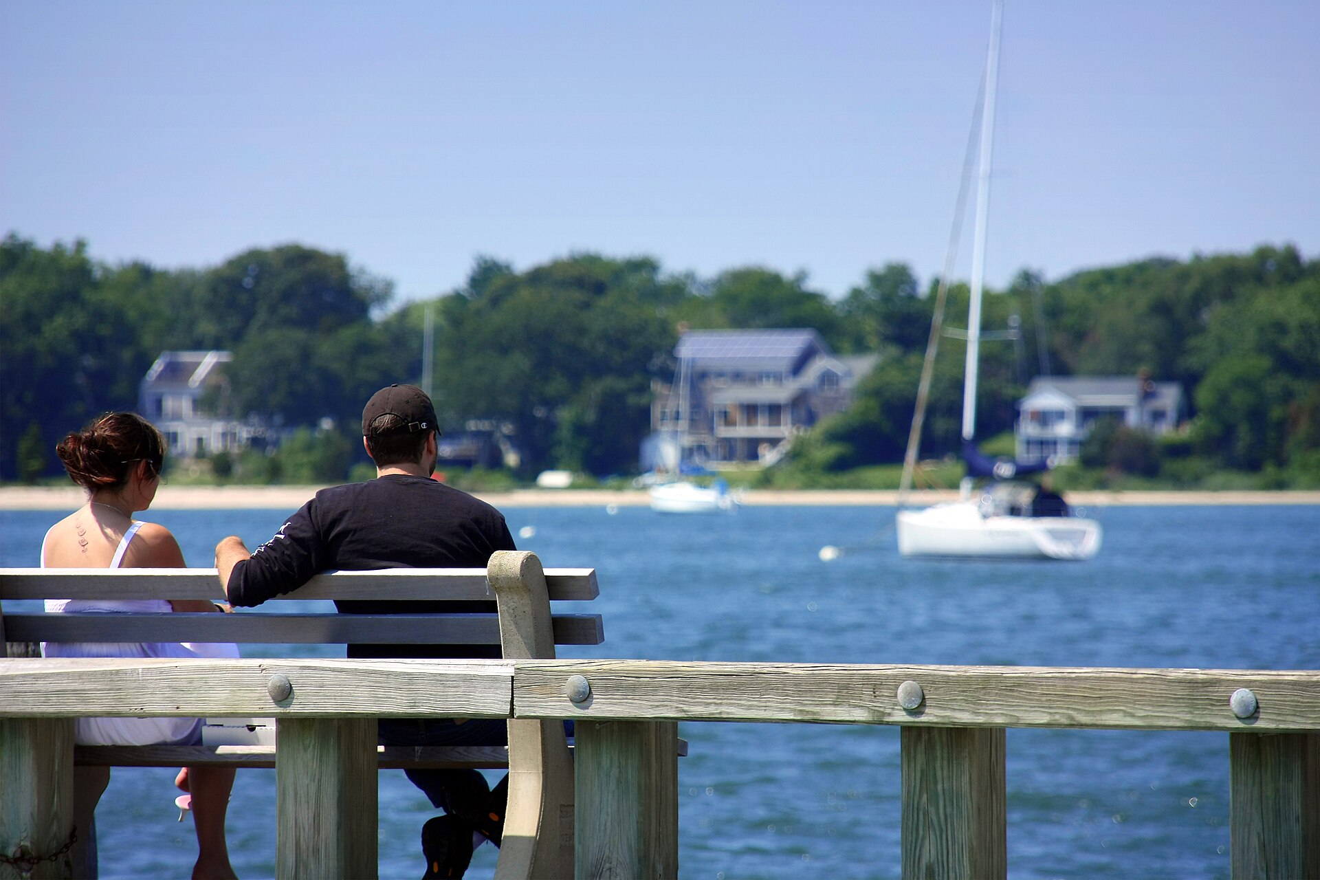 Two people sit at the edge of a quiet dock overlooking Sag Harbor Bay