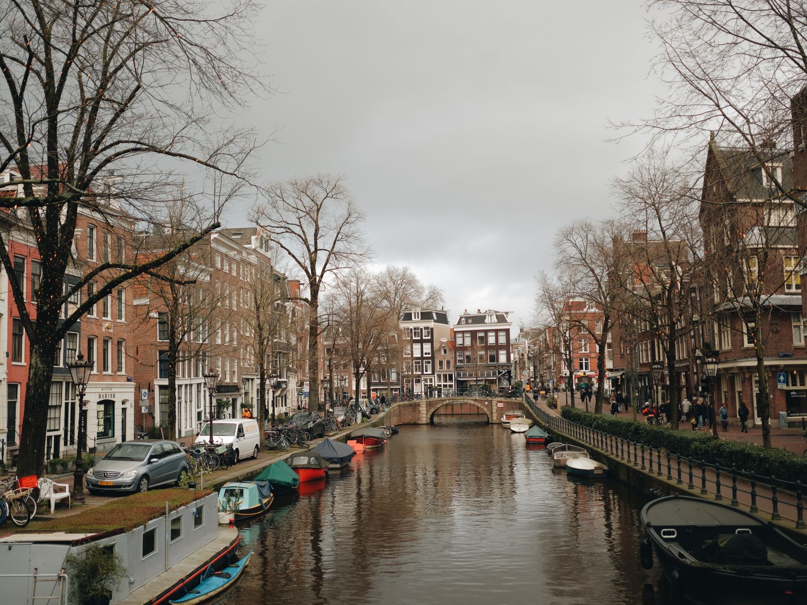 A quiet Amsterdam canal curves beneath bare winter trees and brick canal houses
