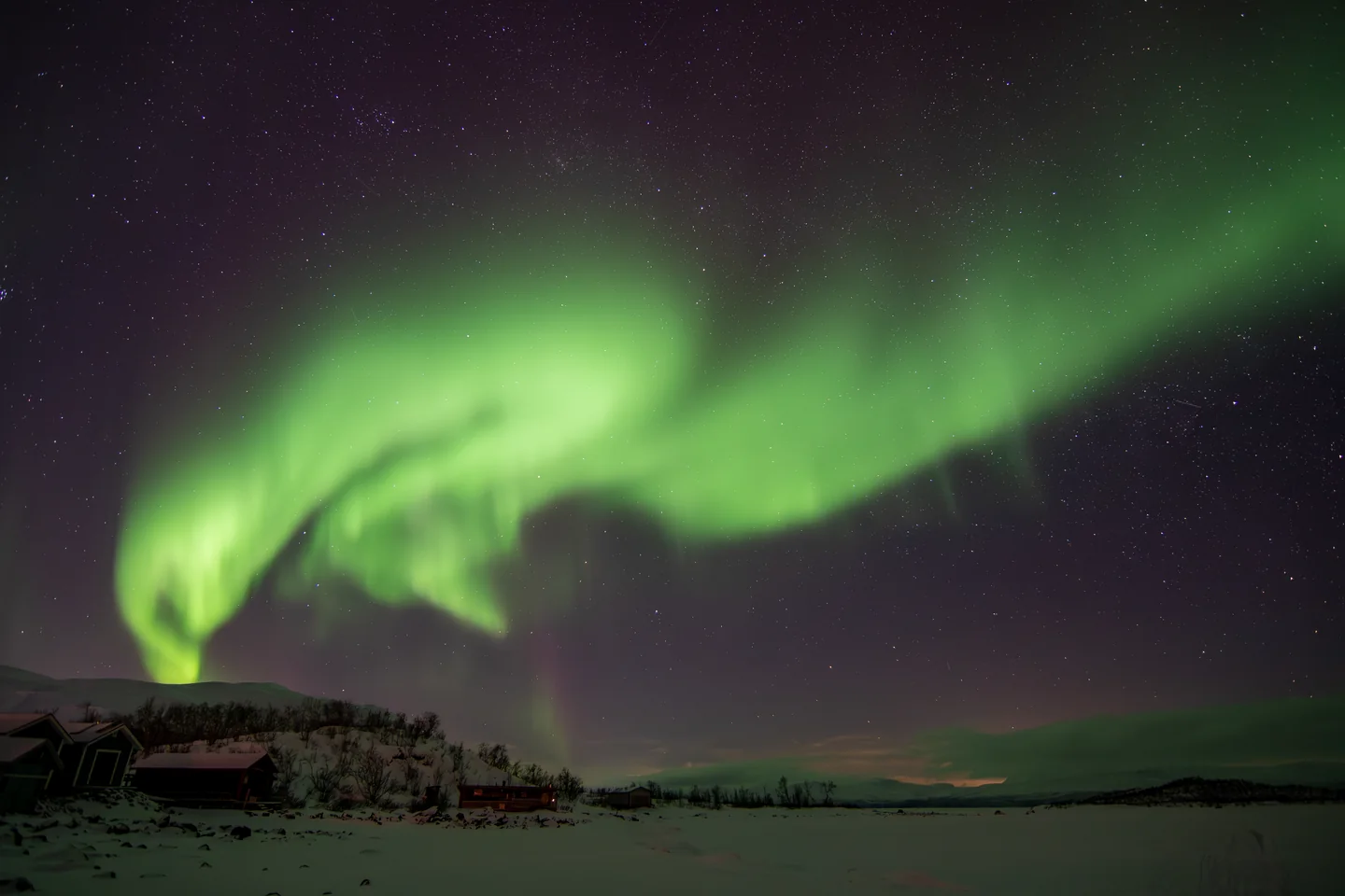 Aurora over snowy buildings and mountains in Abisko National Park, Sweden