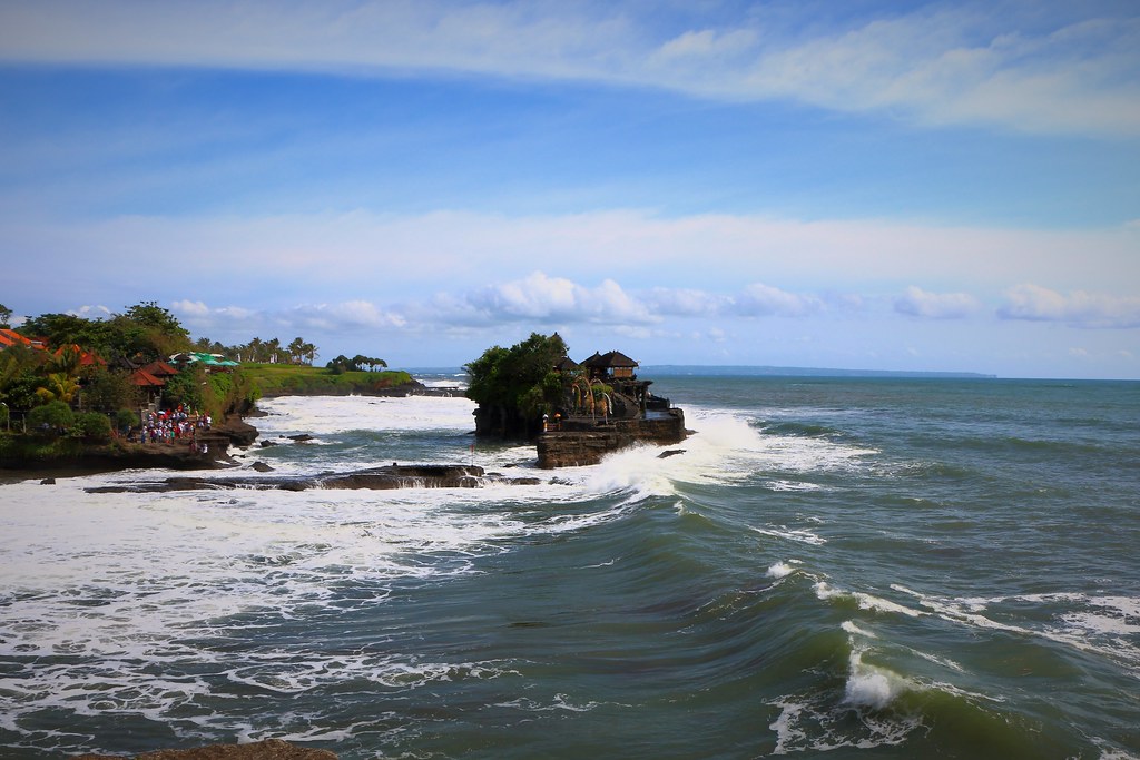 Tanah Lot temple sits on a rocky coastline in Bali with waves below