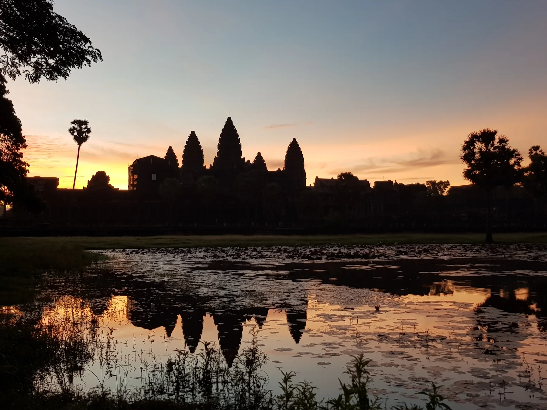 Angkor Wat towers reflected in water beneath the brightening dawn sky
