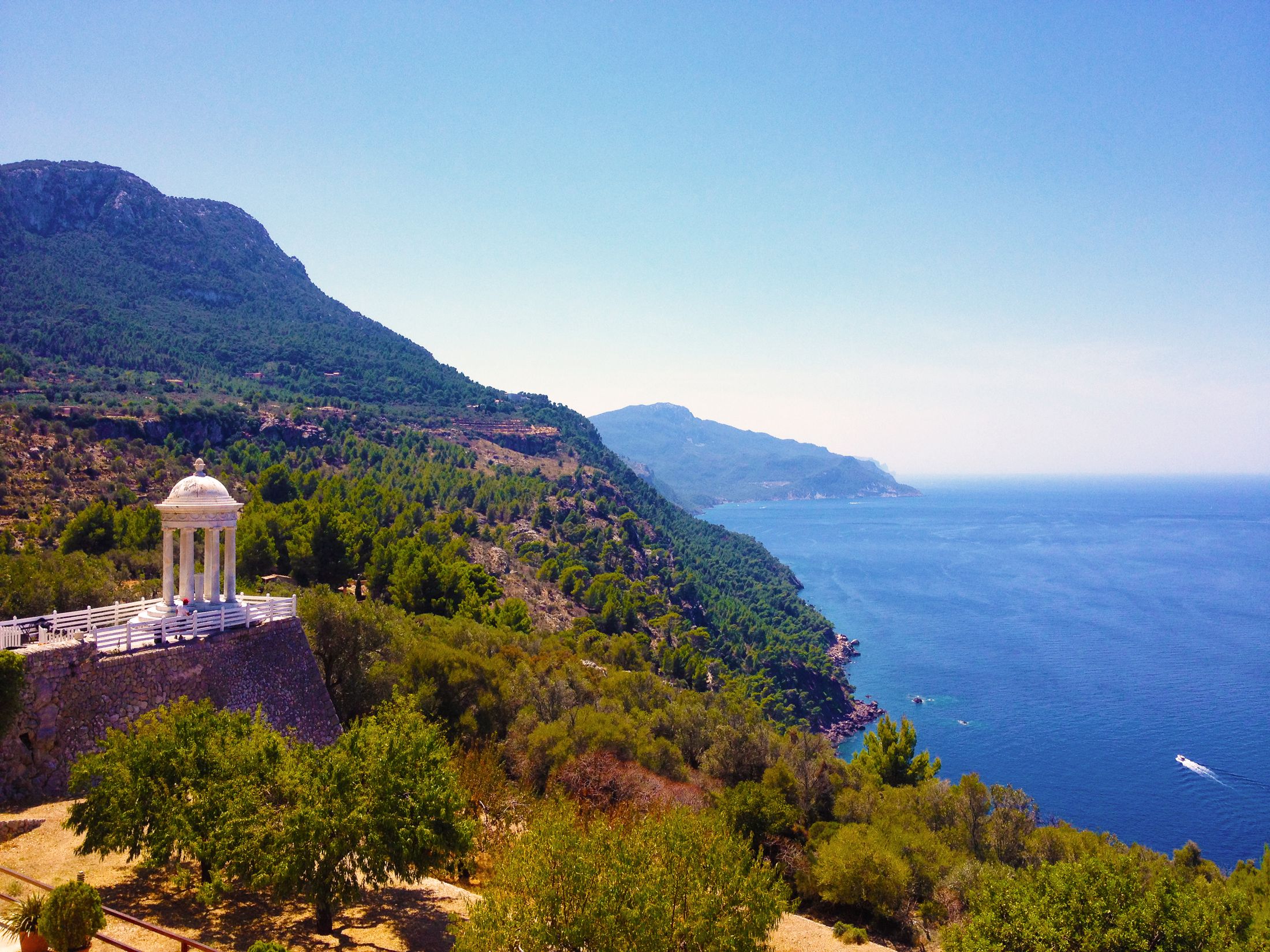 A Mediterranean coastline curves below a sunlit terrace and blue sea
