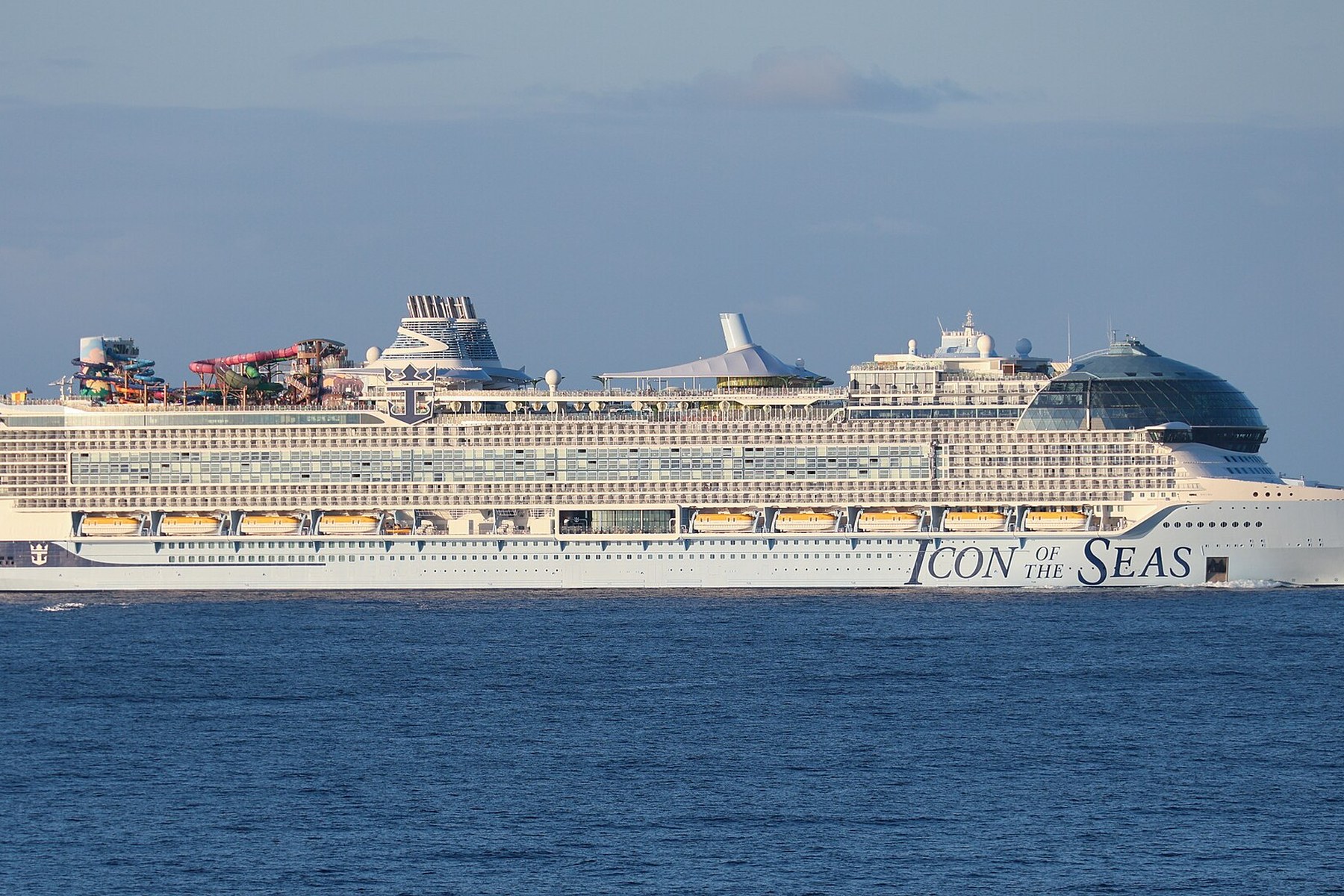 A large modern cruise ship sails across calm blue water