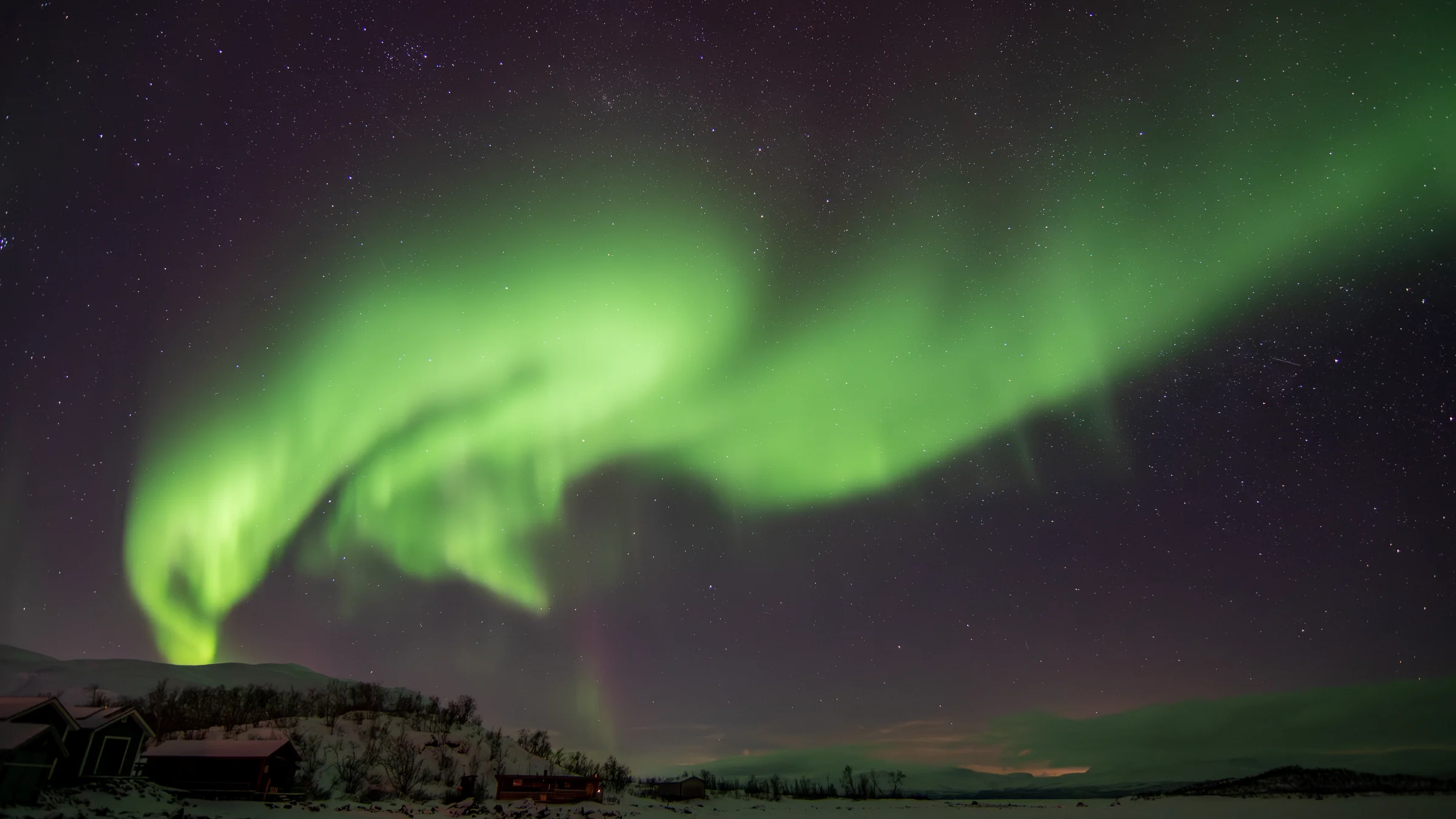 Aurora above snowy buildings and mountains in Abisko National Park